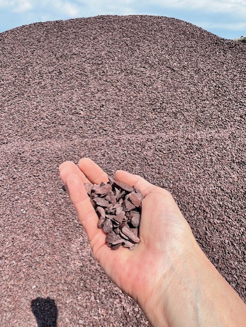 Handful of red decorative gravel in front of a stockpile